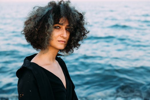 Portrait of a young woman with curly hair by the sea, exuding natural beauty and authenticity.